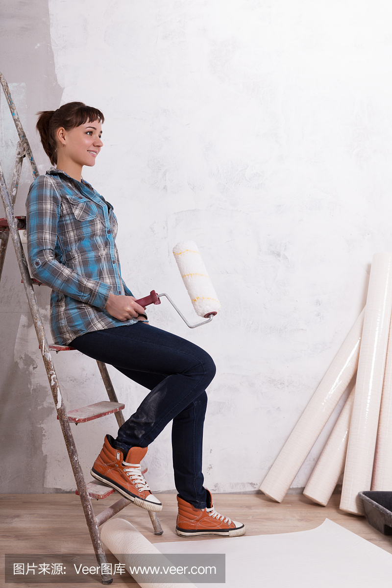 漂亮的女人与辊粘贴壁纸修理房子