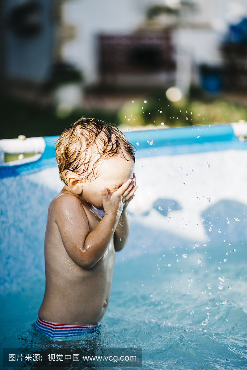 小男孩站在一个划水池里用手遮住眼睛