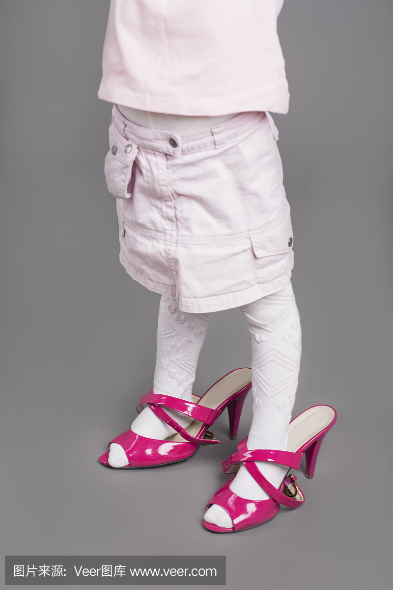 试穿母亲的不合适的高跟鞋的小女孩的腿的特写