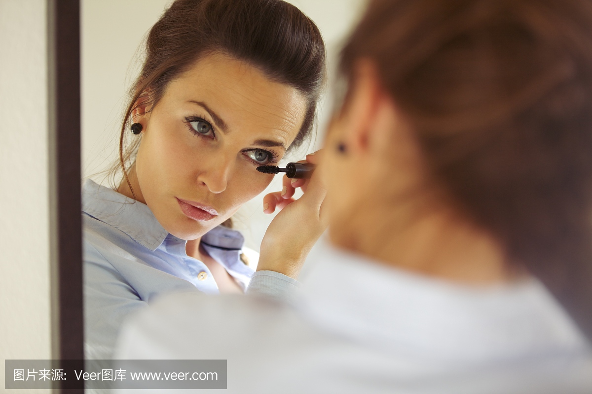 女企业家在镜子中应用睫毛膏