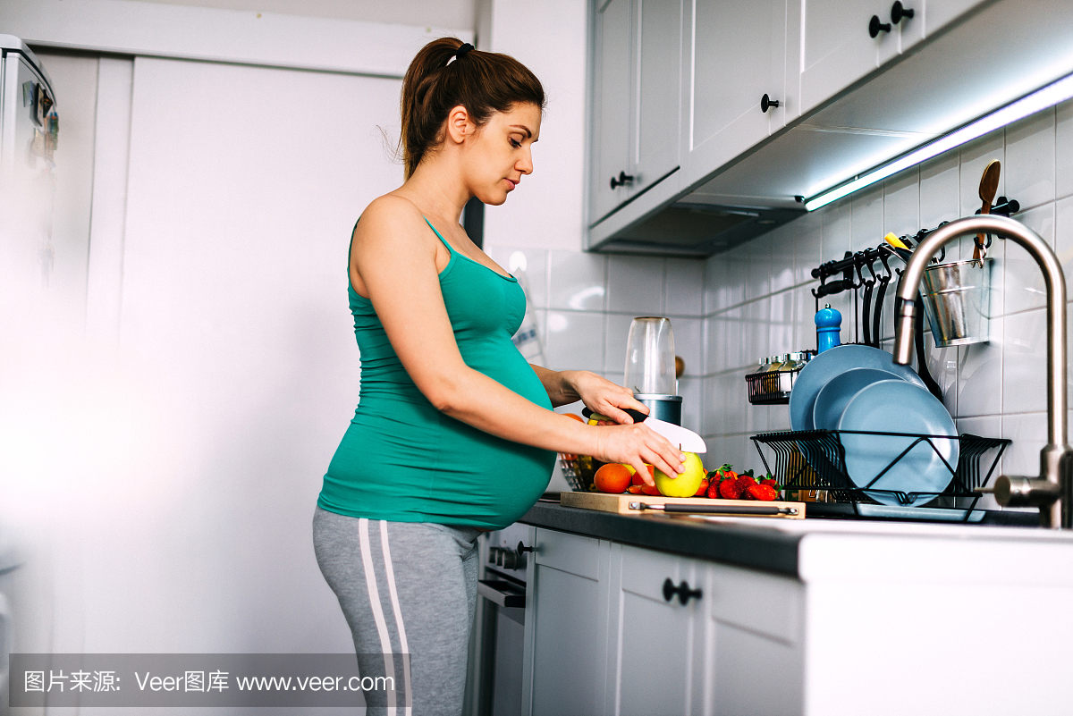 千禧年九个月孕妇在家里,在厨房里准备果汁