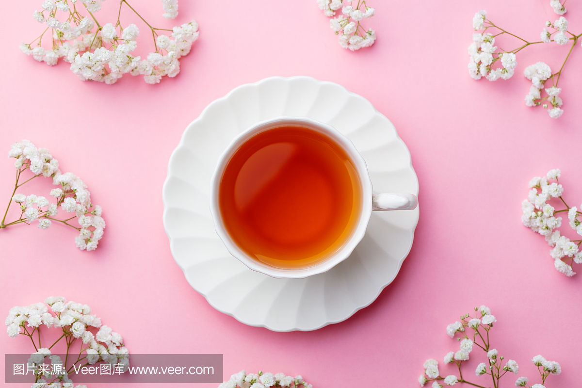 喝杯茶与粉红色的背景上的鲜花。顶视图。复制
