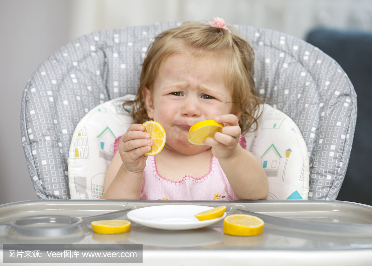 快乐宝贝女孩在高脚椅里吃柠檬。