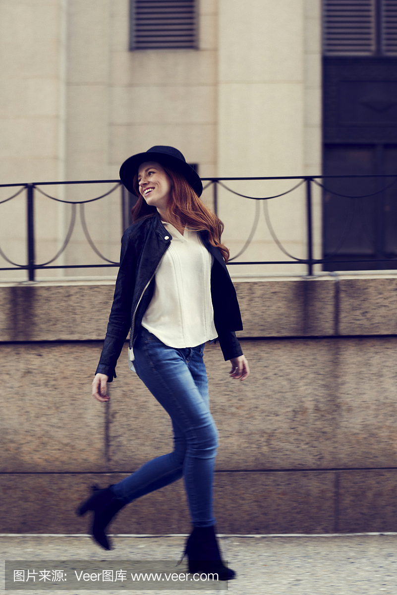 穿牛仔裤和帽子的年轻妇女走在纽约街头的栏杆