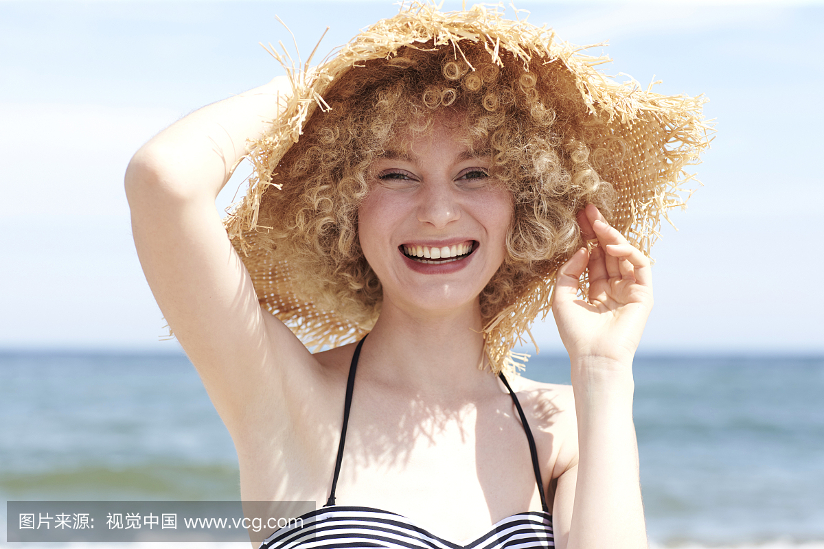 笑在海滩上戴草帽的年轻女子的画像