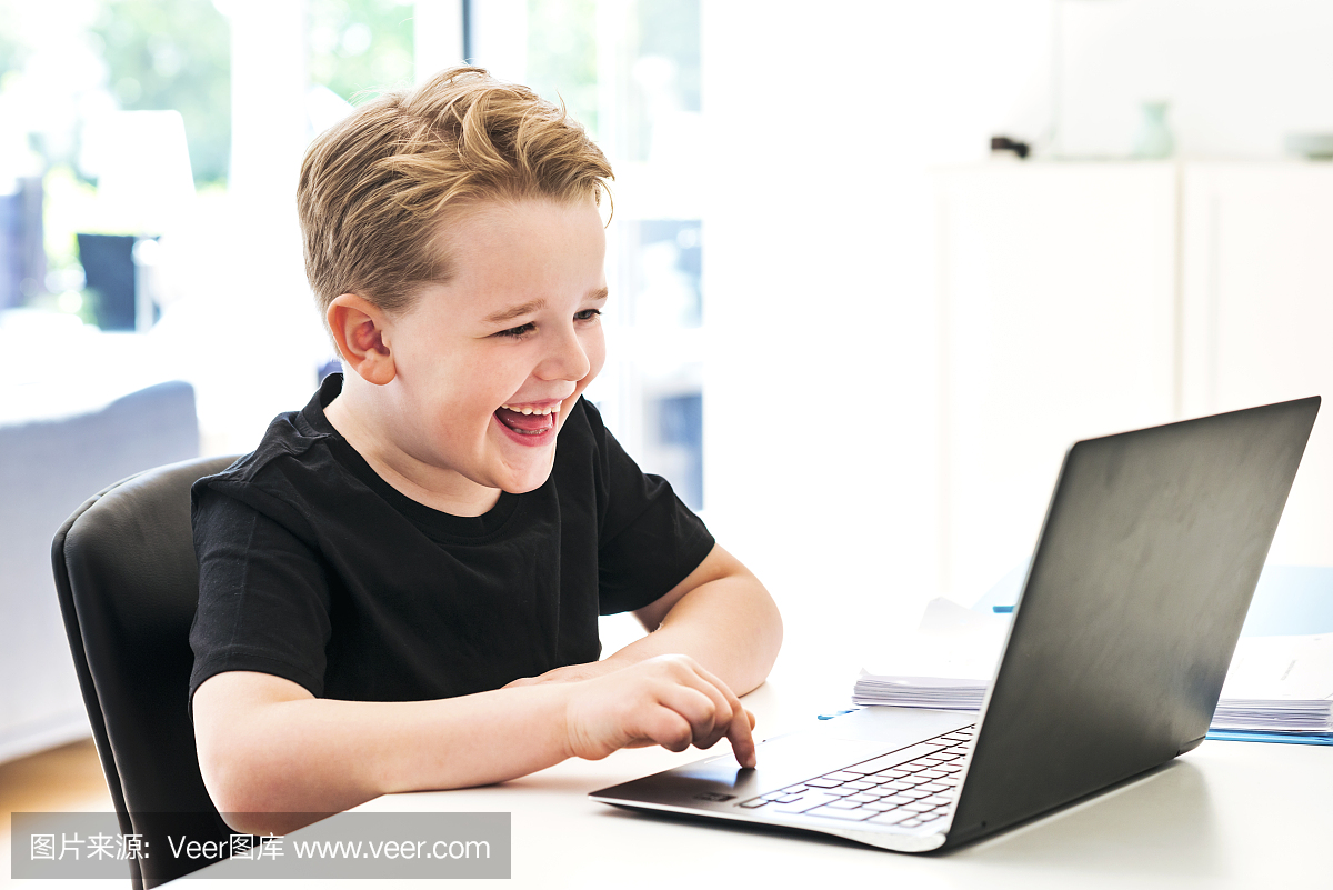 当他在家里在笔记本电脑上打字时,男孩笑了起