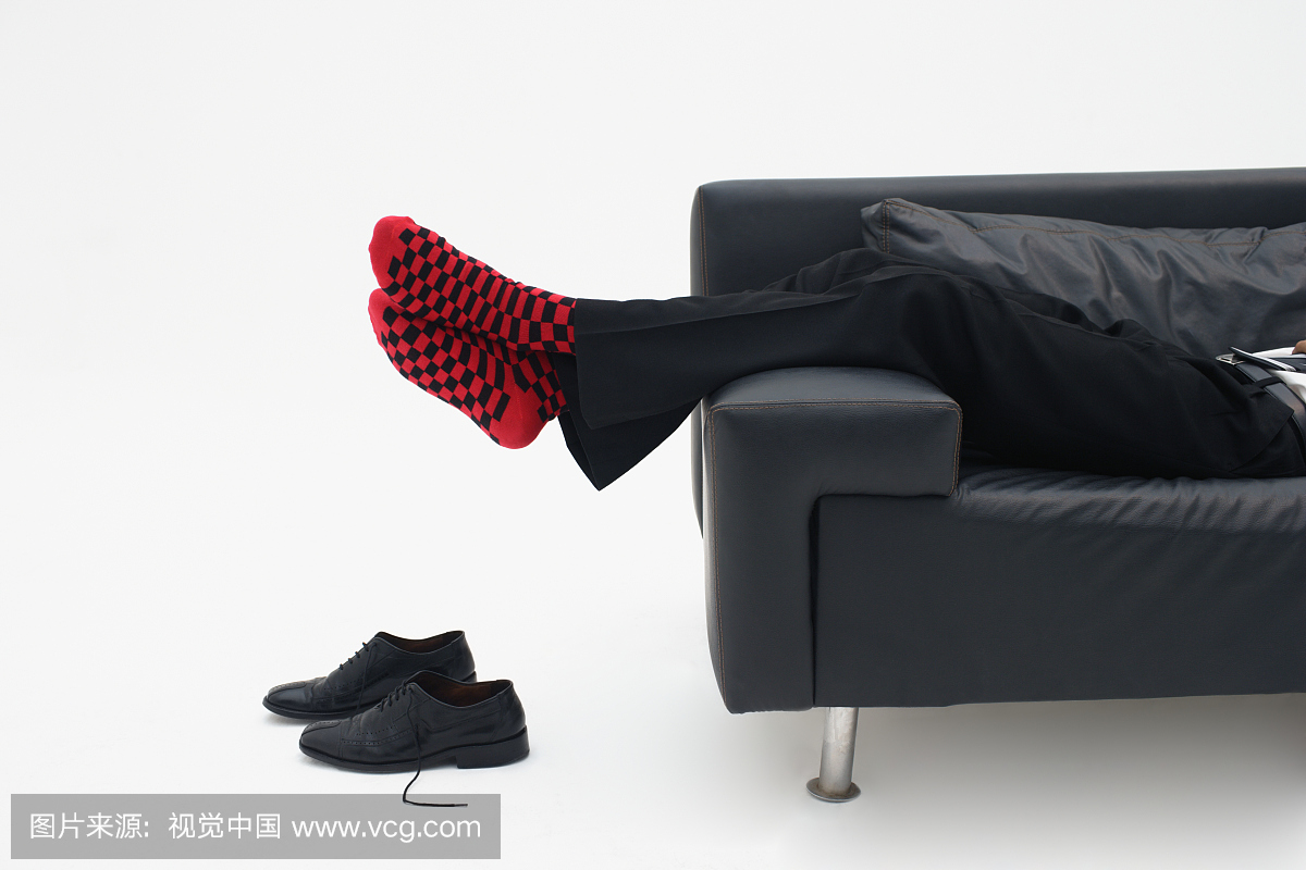 放松在沙发上的商人穿红色检查的袜子,低部分