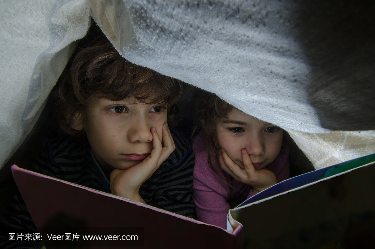睡觉前,小男孩和女孩在床单下阅读