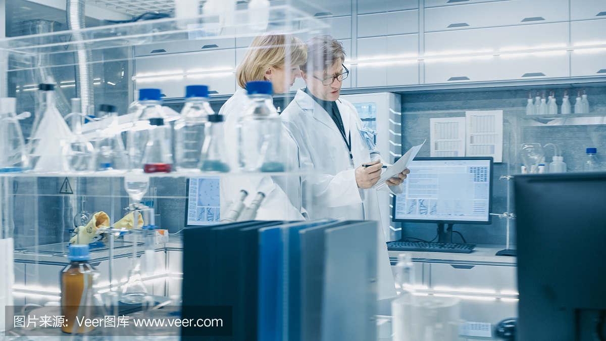 女性和男性高级科学家走过繁忙的现代实验室。