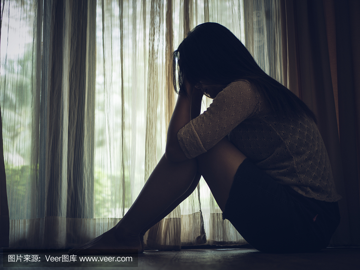 悲伤的女人独自坐在窗户或门旁的空房间里