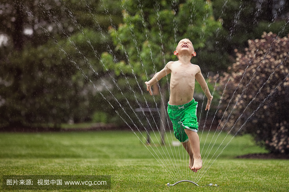 小男孩跳过花园喷水器