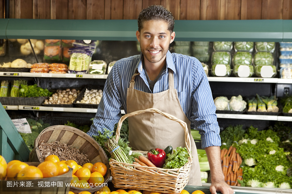一个快乐的年轻推销员与蔬菜篮子在超市的肖像