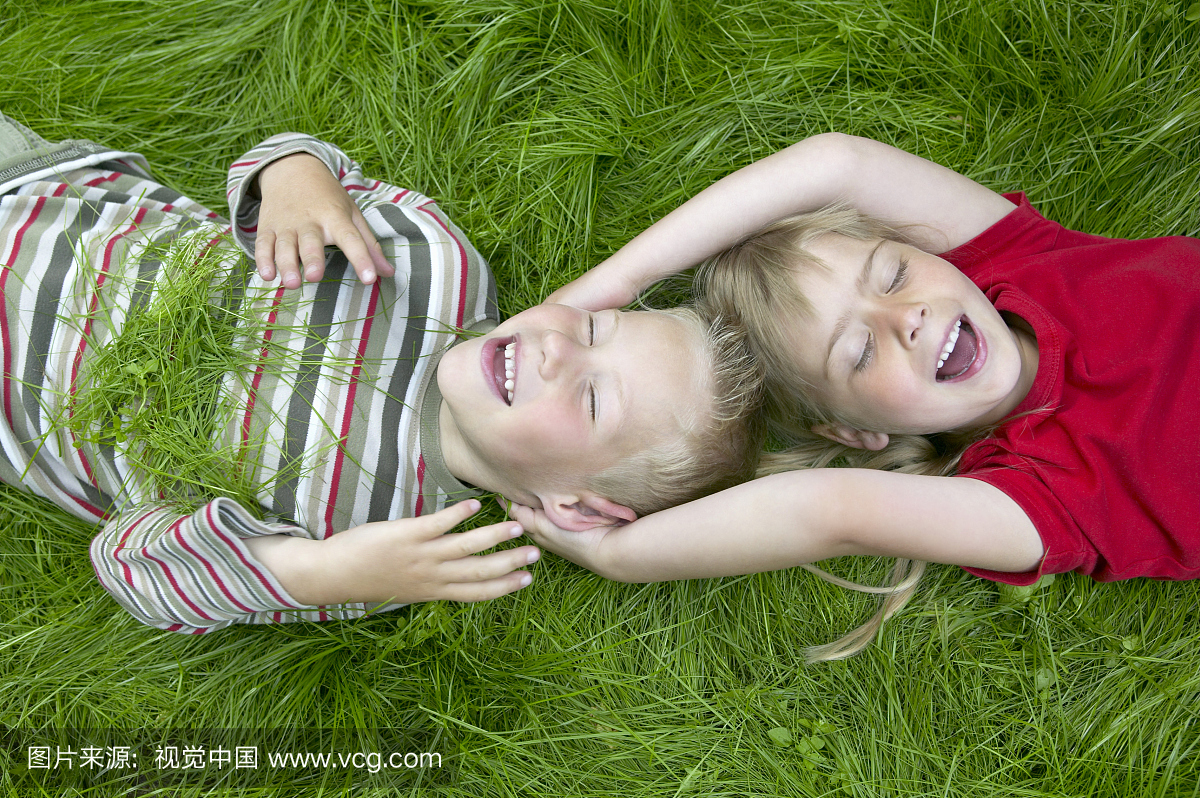 男孩和女孩(4-6)躺在草地上笑,女孩触摸男孩的