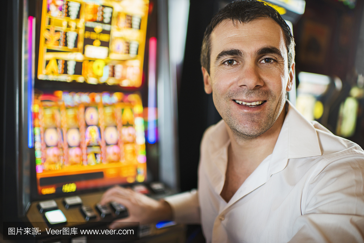 在娱乐场的老虎机赌博的微笑的男人。