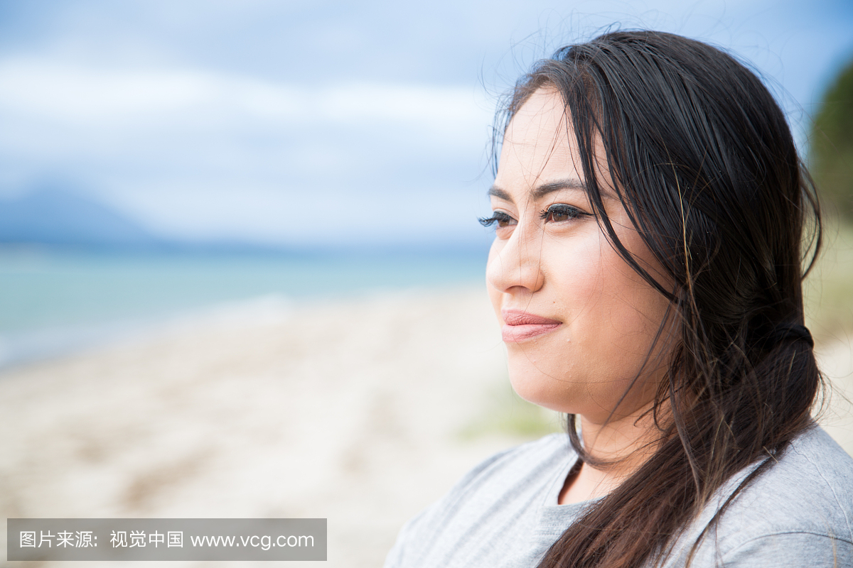 毛利人的女人站在望着大海的沙滩上