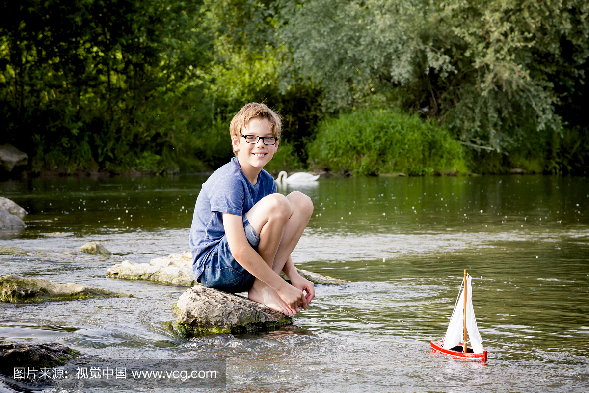 男孩玩在一条河上的木玩具船