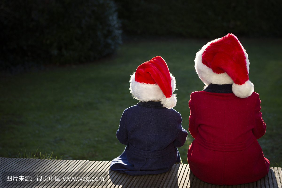 两个孩子坐在户外与圣诞老人的帽子