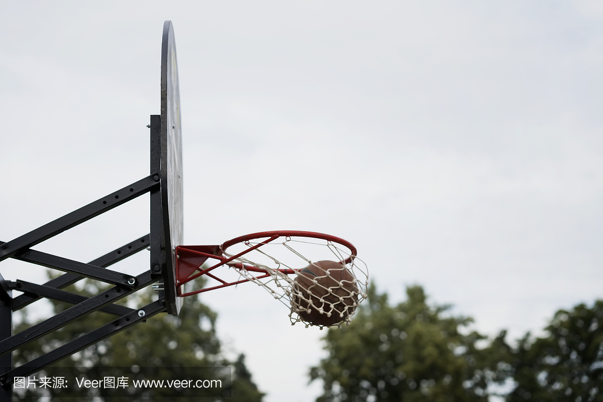 街头篮球比赛。篮球盾牌,球穿过天空,树木的背