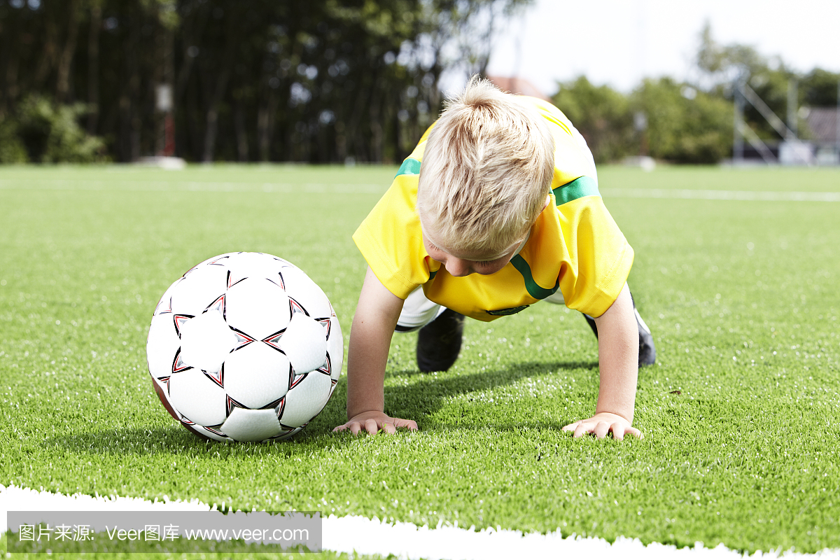 四岁的男孩在一个足球旁边做俯卧撑