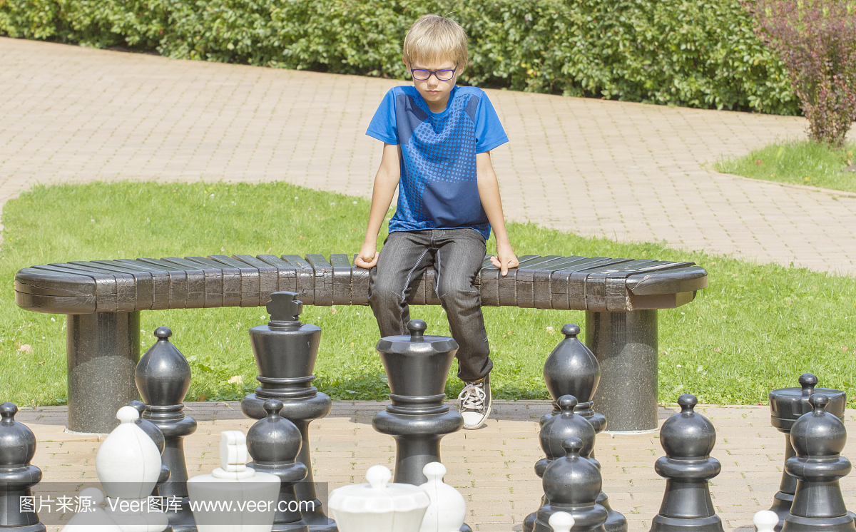 集中的小孩玩户外象棋游戏使用生活大小的国际象棋