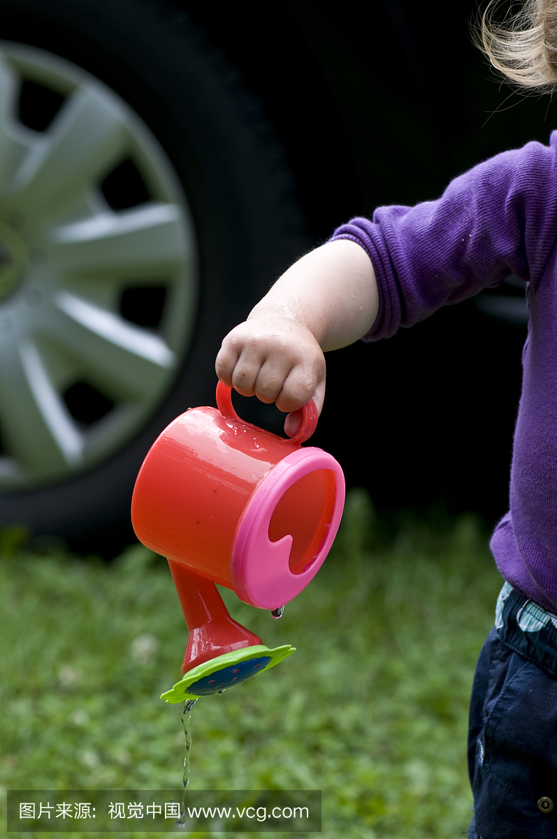 一个女孩的手臂,一岁半,玩塑料玩具浇水罐