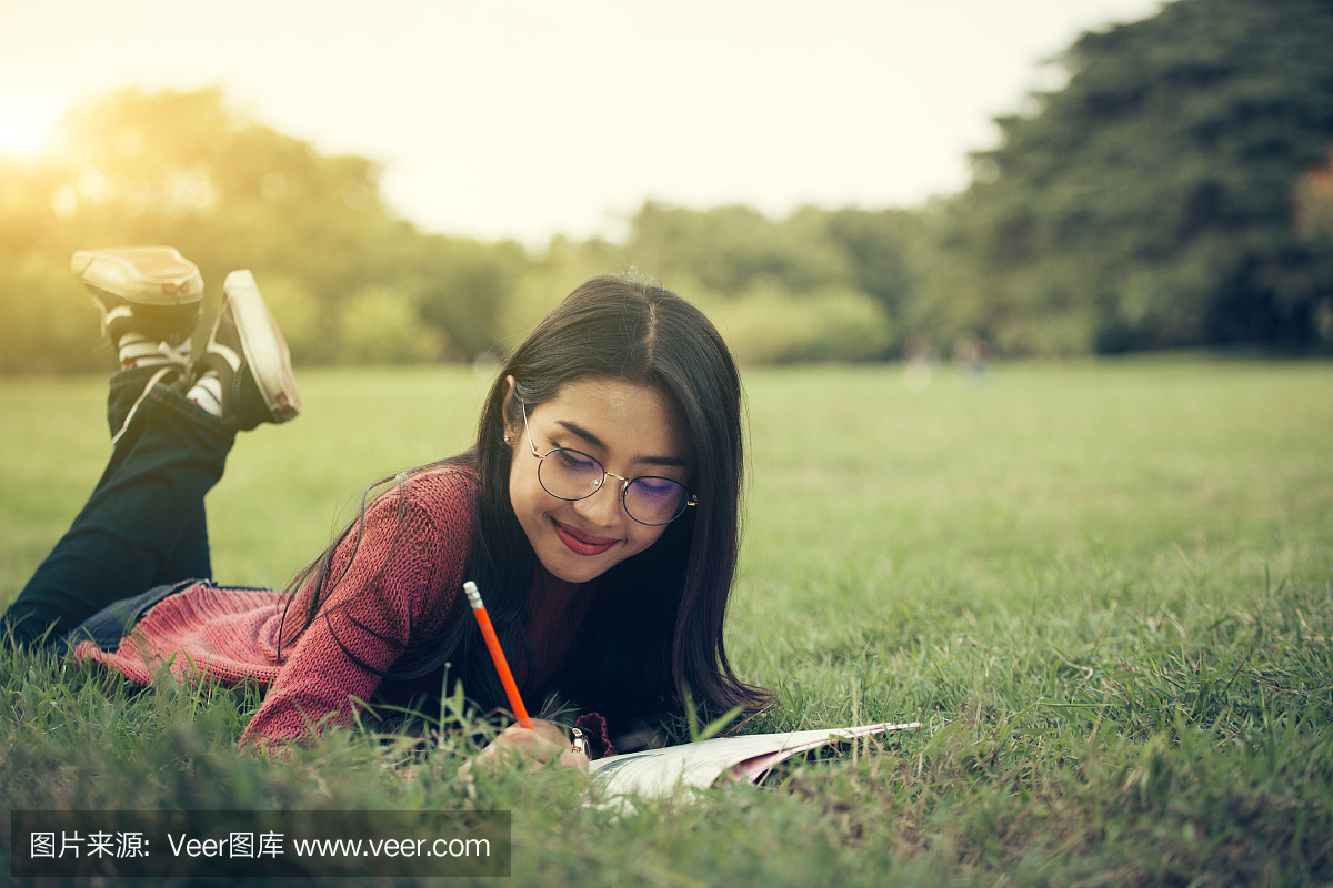 高中女生的肖像躺下来读一本书在公园里,教育