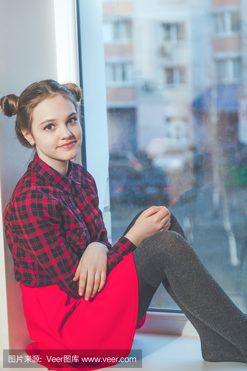 坐在窗台上的红色裙子的青少年的女孩