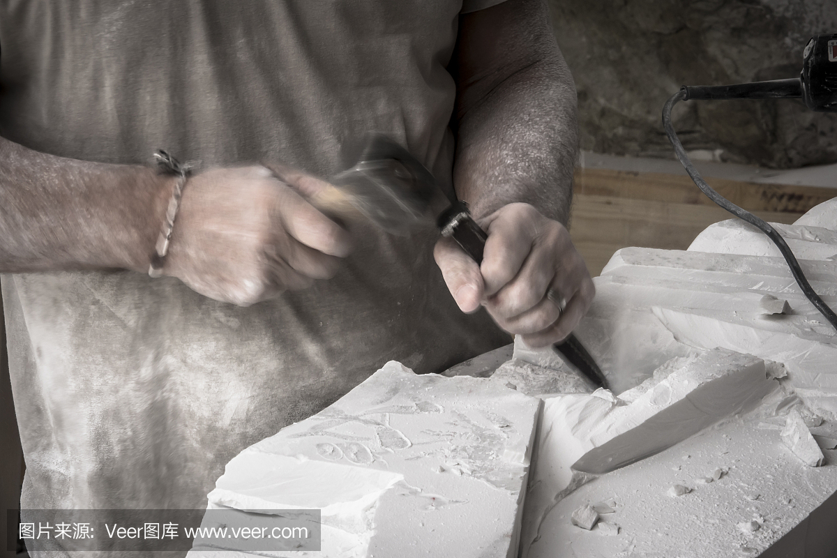 用锤子和凿子雕刻大理石的艺术家的手的细节