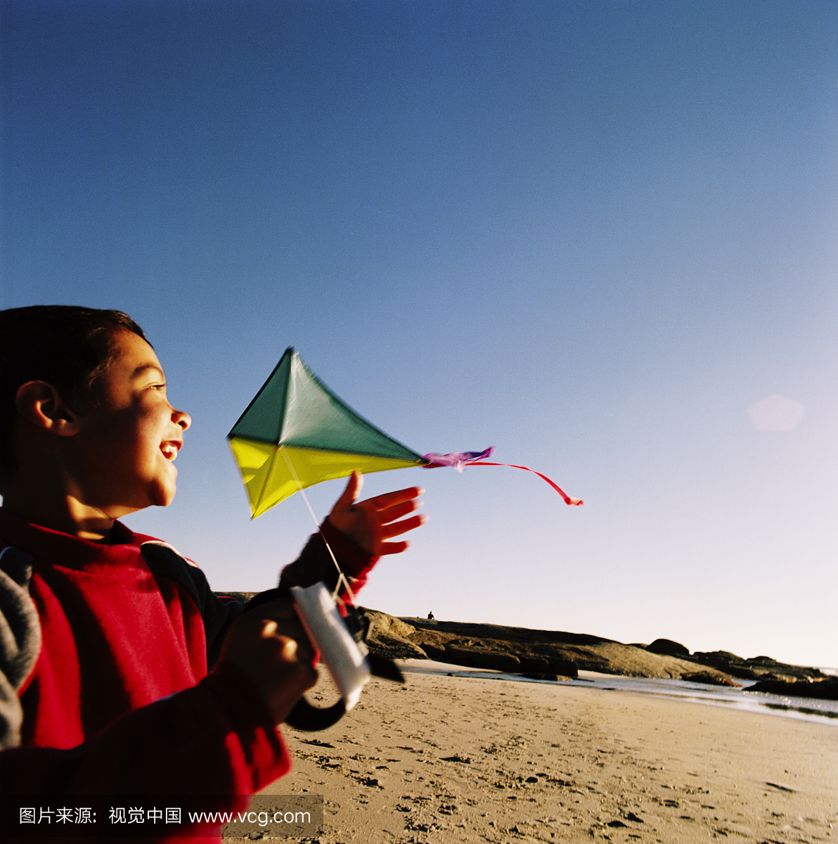 一个年轻男孩(8-10)在海滩上放风筝的侧面