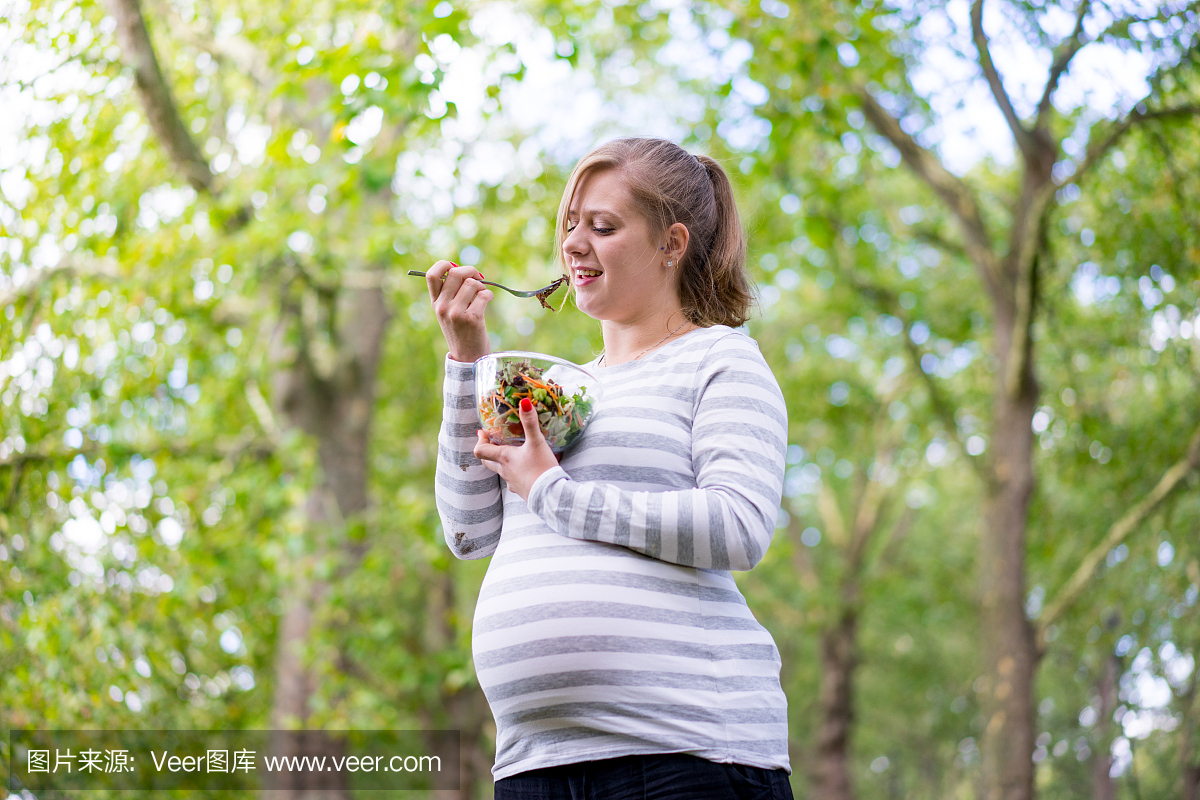 快乐和年轻的孕妇在公园吃食物