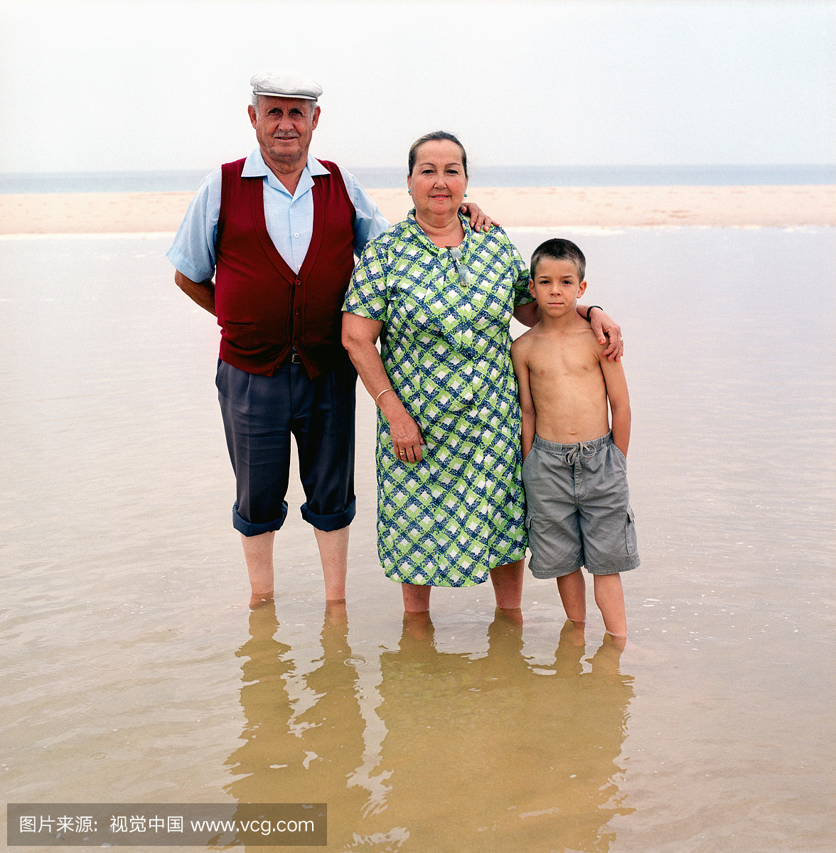 男孩(5-7)在海滩上与祖父母,肖像