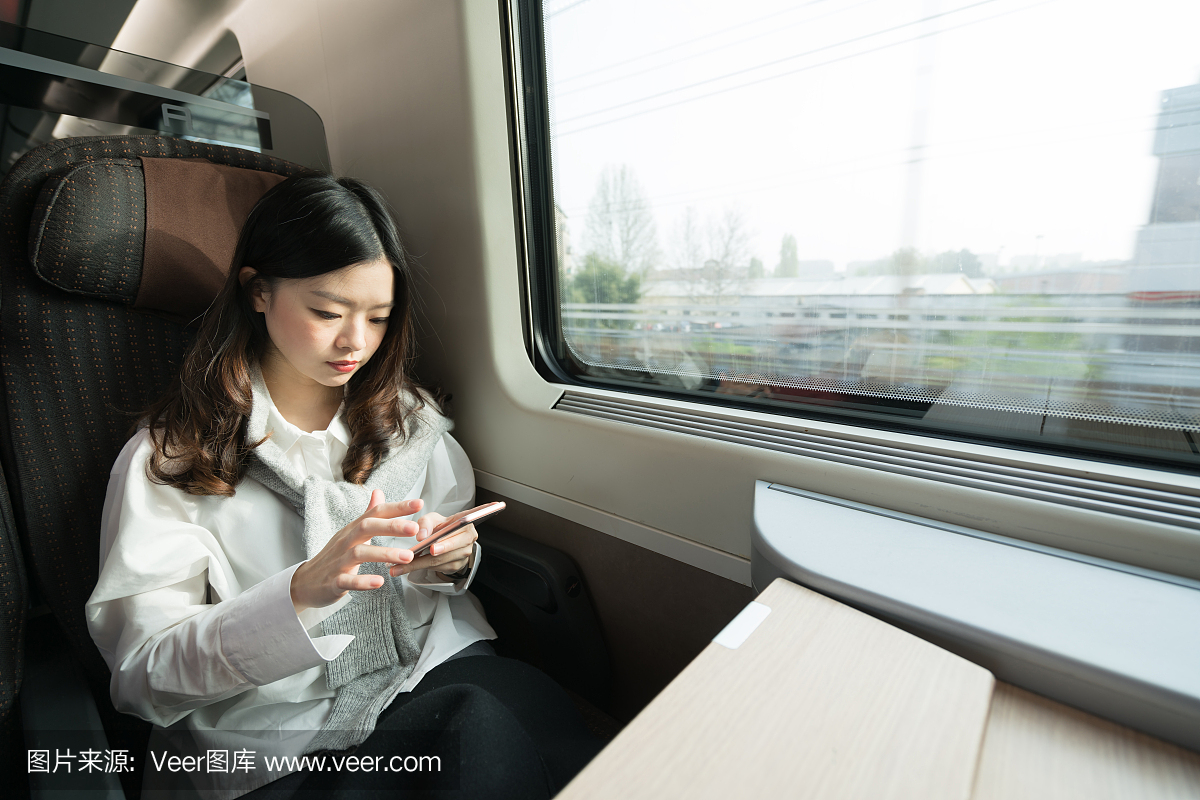 美丽的亚裔女孩在火车上旅行时使用智能手机