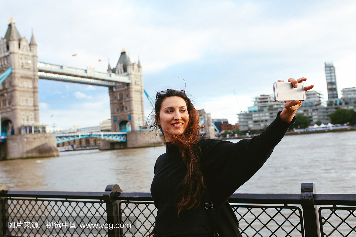 年轻的旅游女人在伦敦塔桥附近采取自拍照
