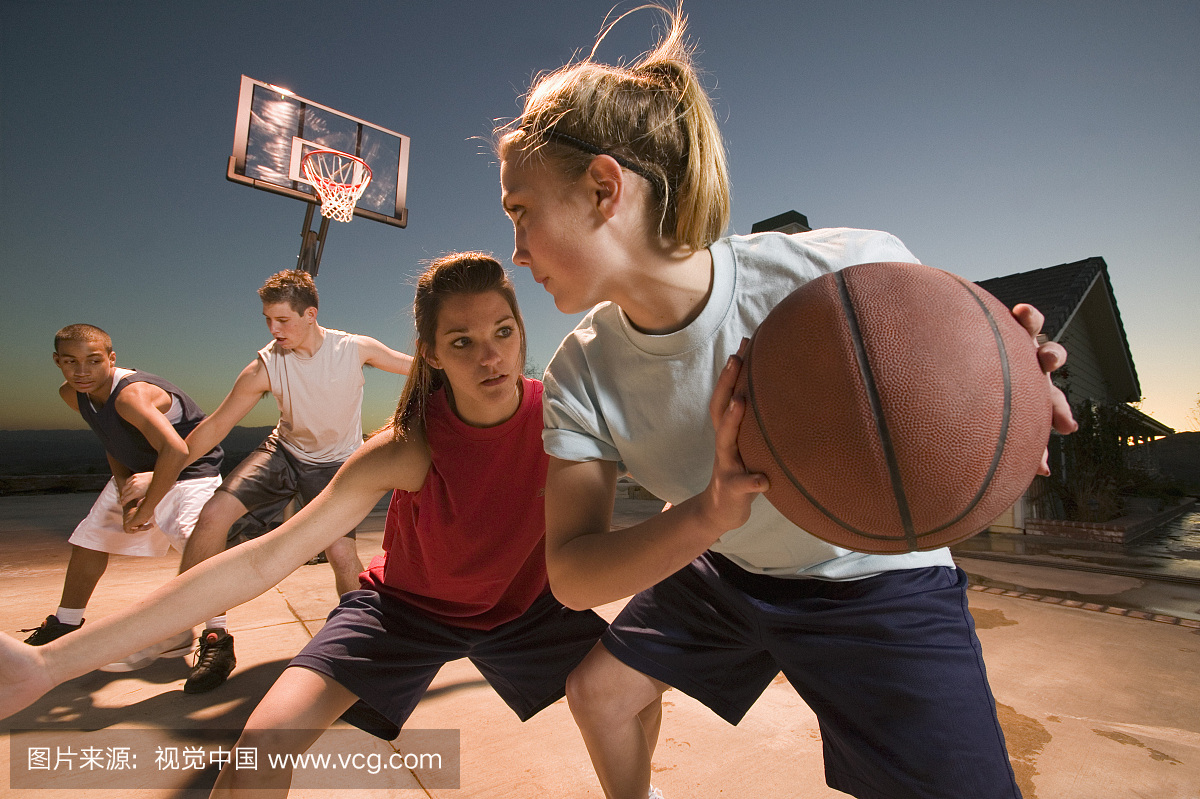 十几岁的女孩和男孩在日落时打篮球