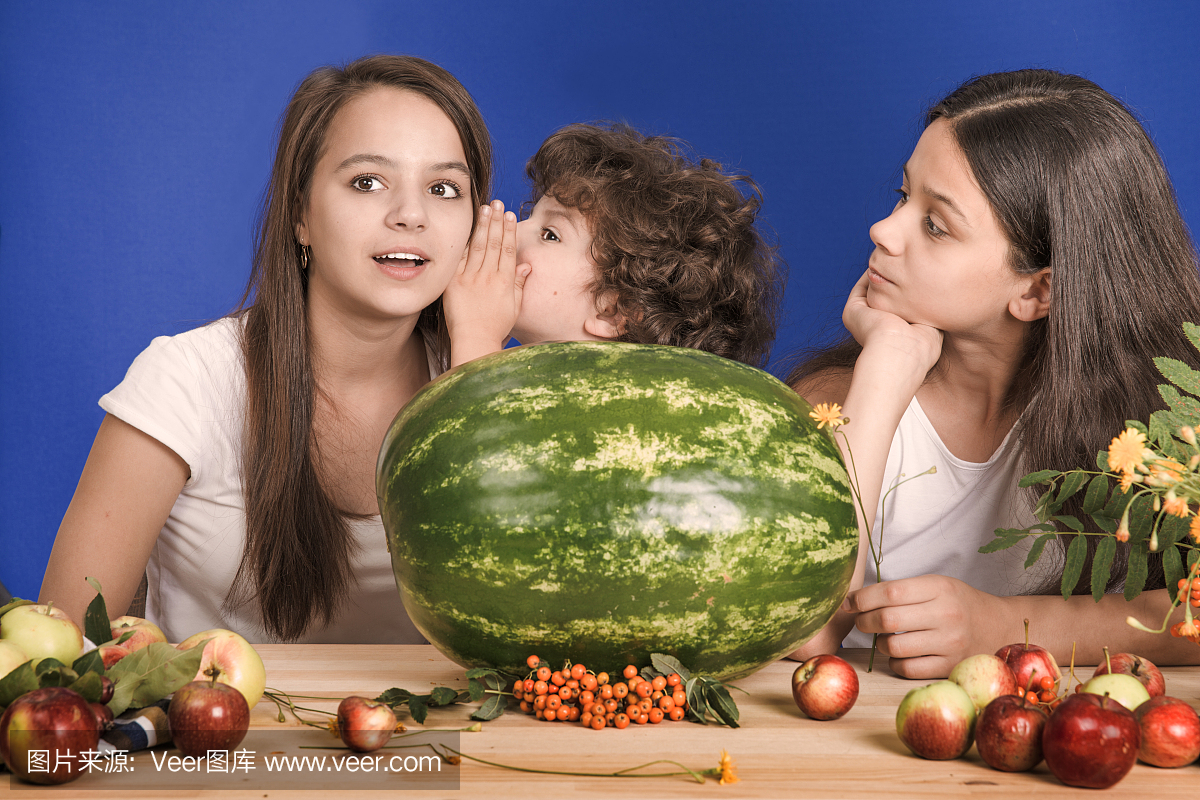 孩子们坐在桌子旁说话,一个大的西瓜