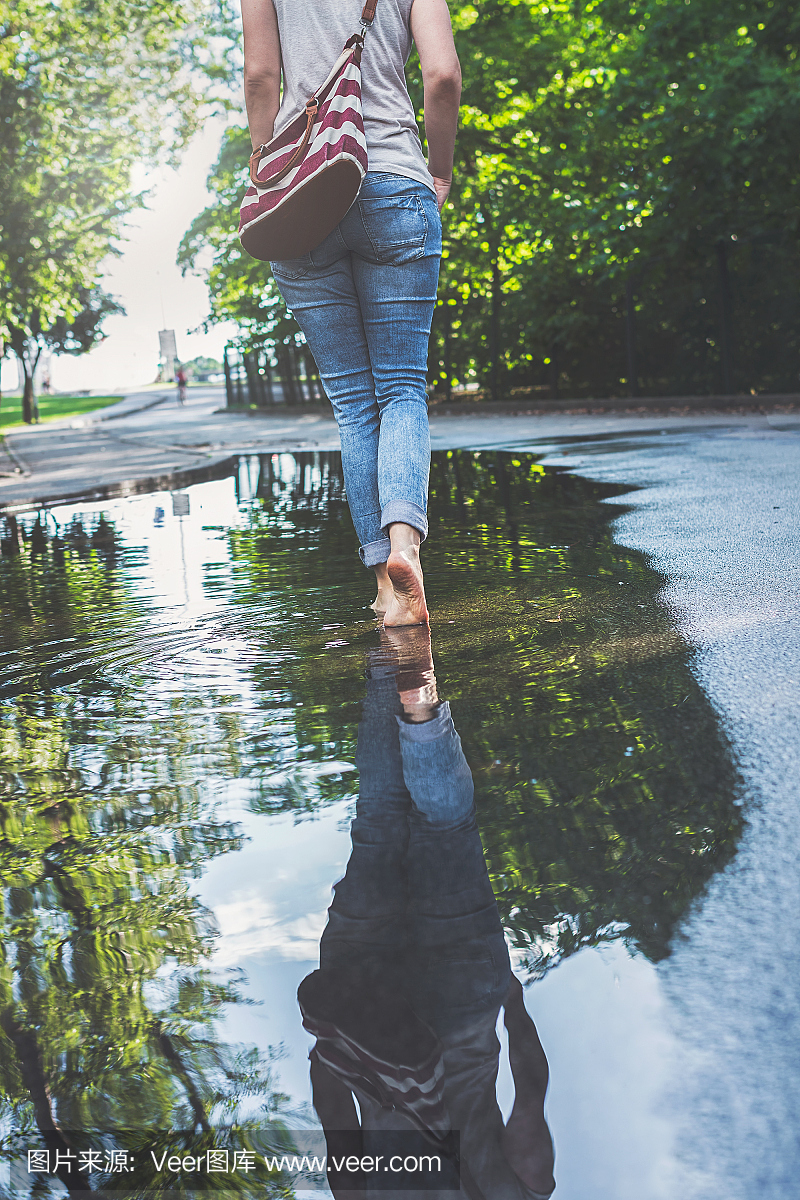 蓝色牛仔裤的赤脚女子在城市环境中穿过水坑