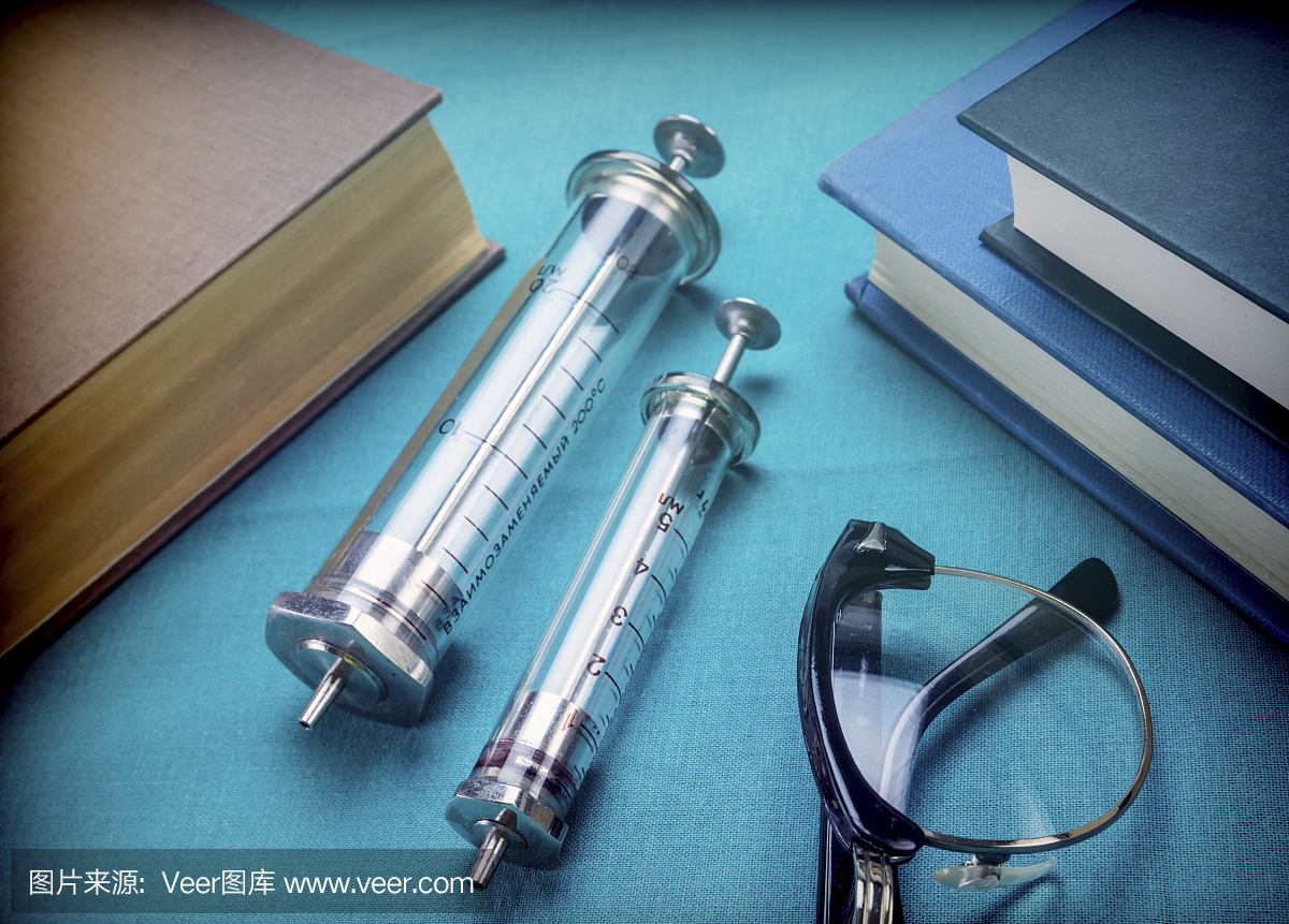 医学书籍老式注射器和眼镜,概念性图像旁边
