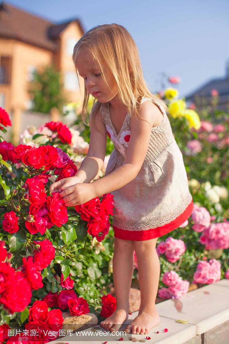 小可爱的女孩坐在花园里的五颜六色的鲜花附近