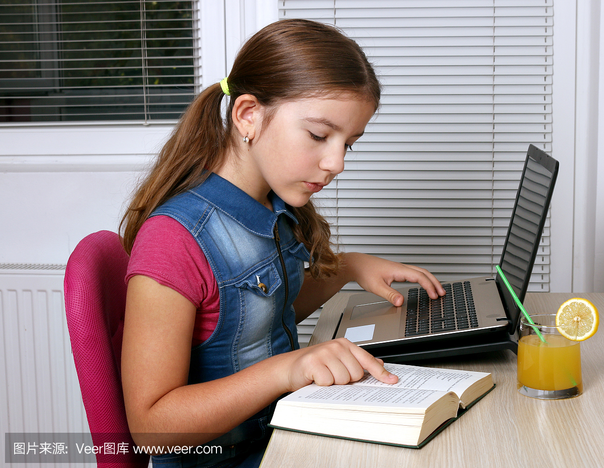 小女孩在家学习一本书和一台笔记本电脑