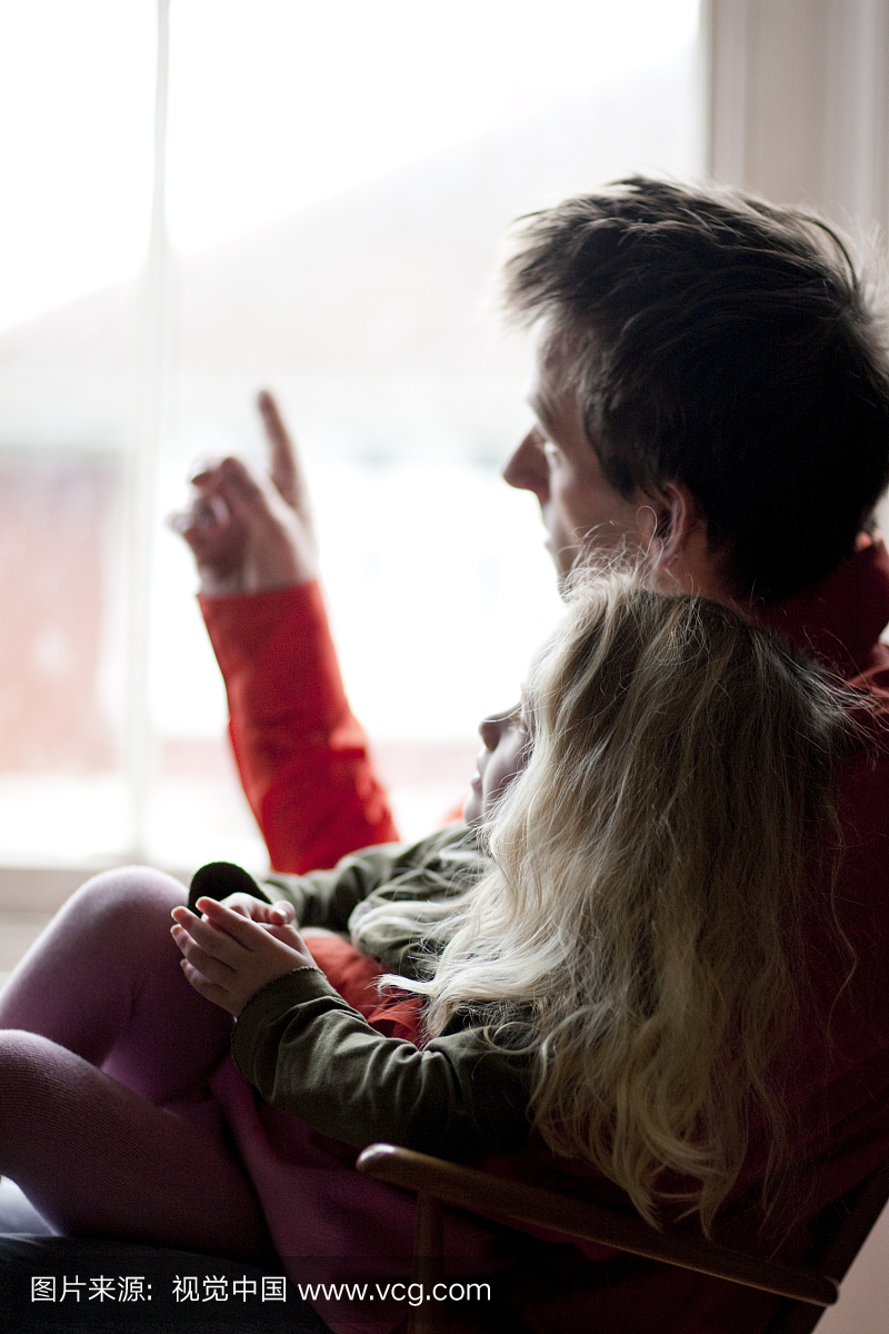 Man with a girl on his lap looking out of a windo