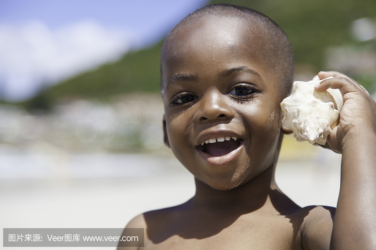 非洲男孩抱着海壳到他的耳朵