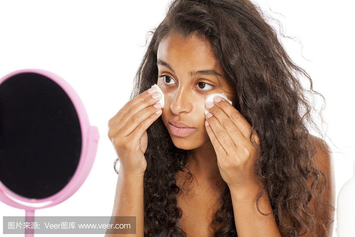 美丽的黑皮肤的女孩用化妆棉清洁她的脸