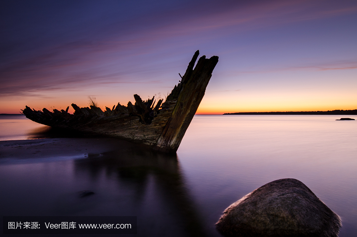 在海滩上的日落与旧的帆船残骸。