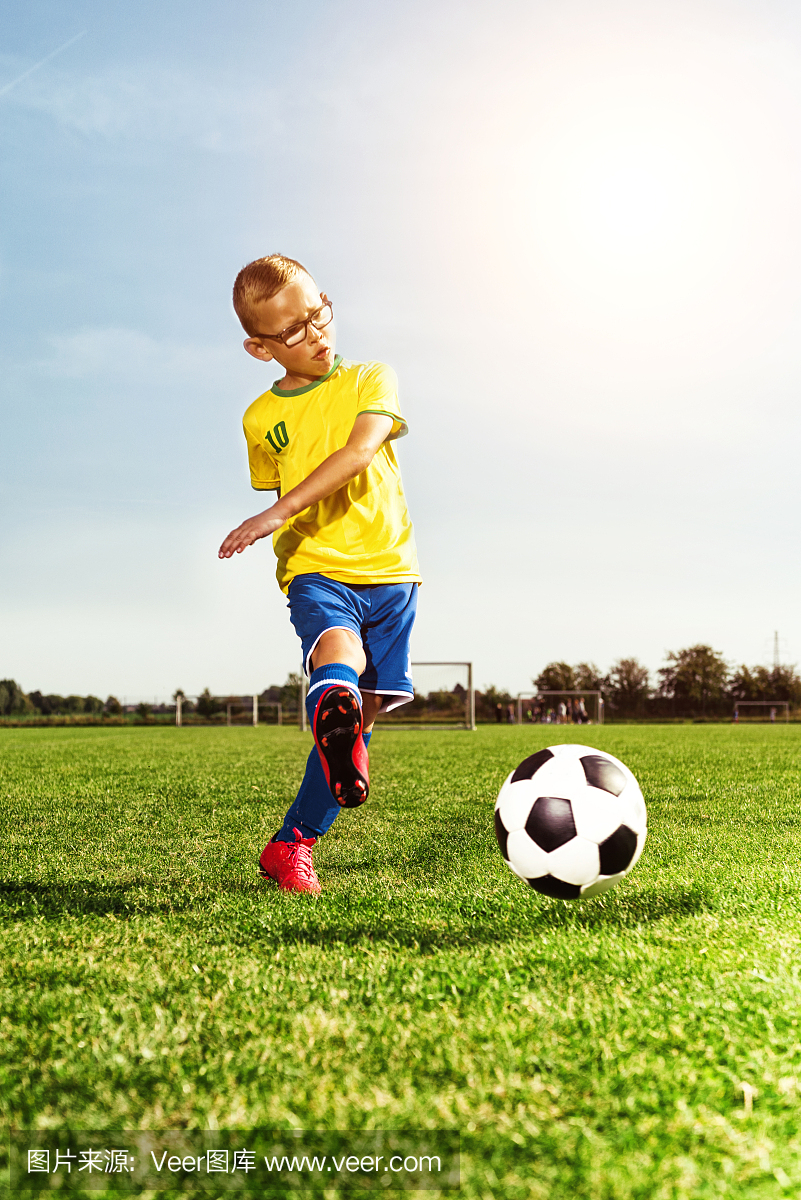 戴眼镜的男孩在运动场上踢足球