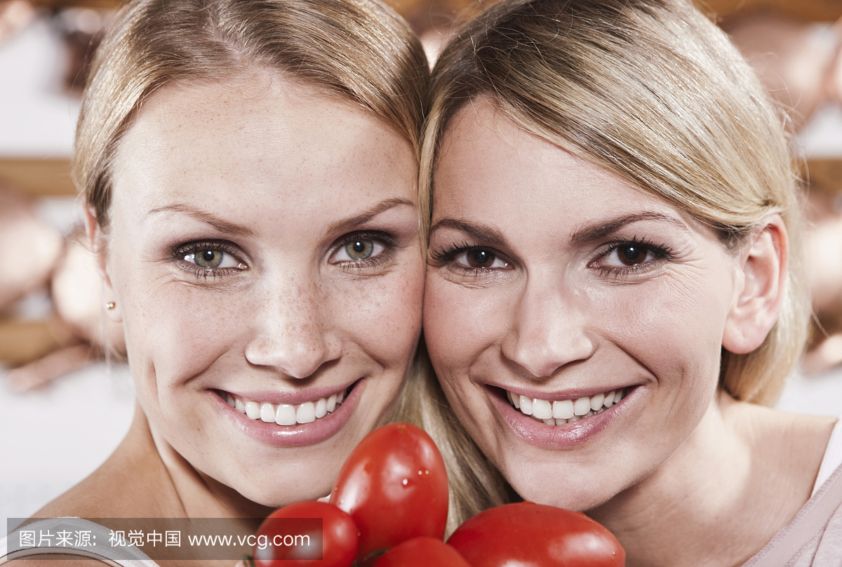 亚诺,关闭两个年轻妇女,在厨房里拿着西红柿,微