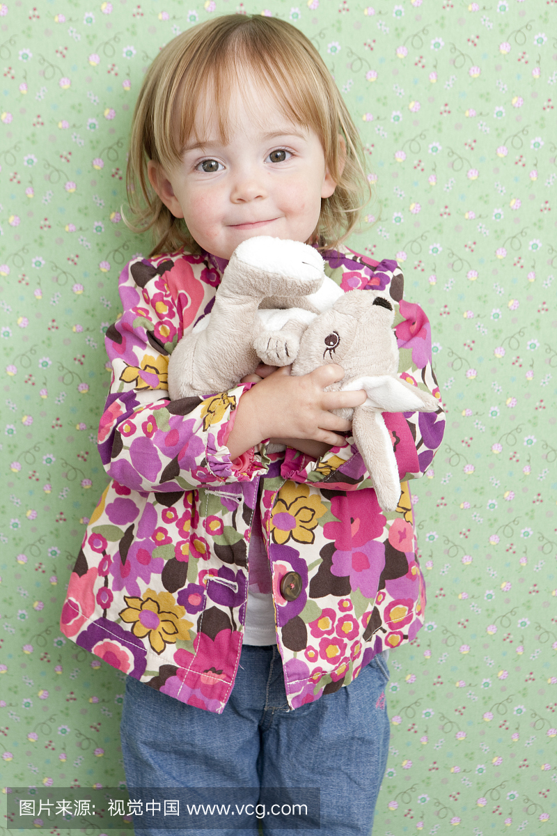 抱抱玩具兔子的五颜六色的外套的小孩的女孩。