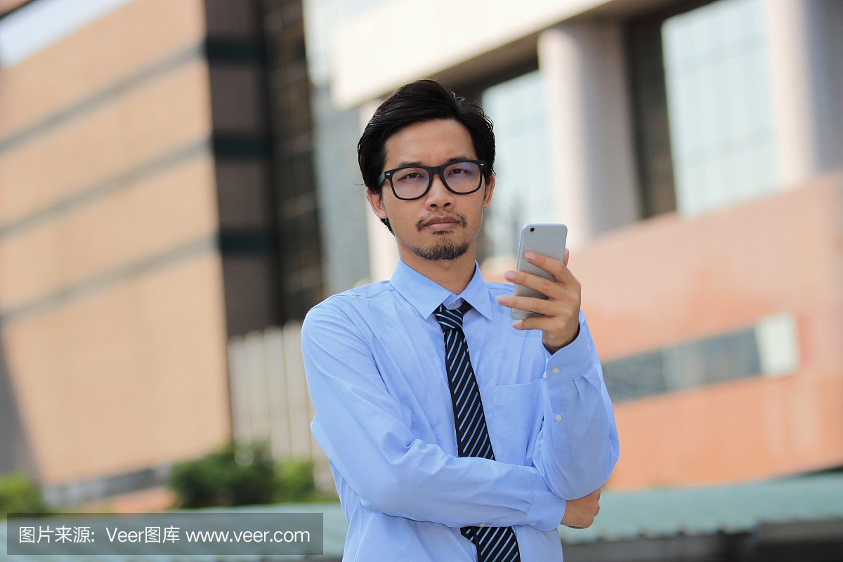 肖像的帅哥年轻亚裔商人持有移动智能手机,并