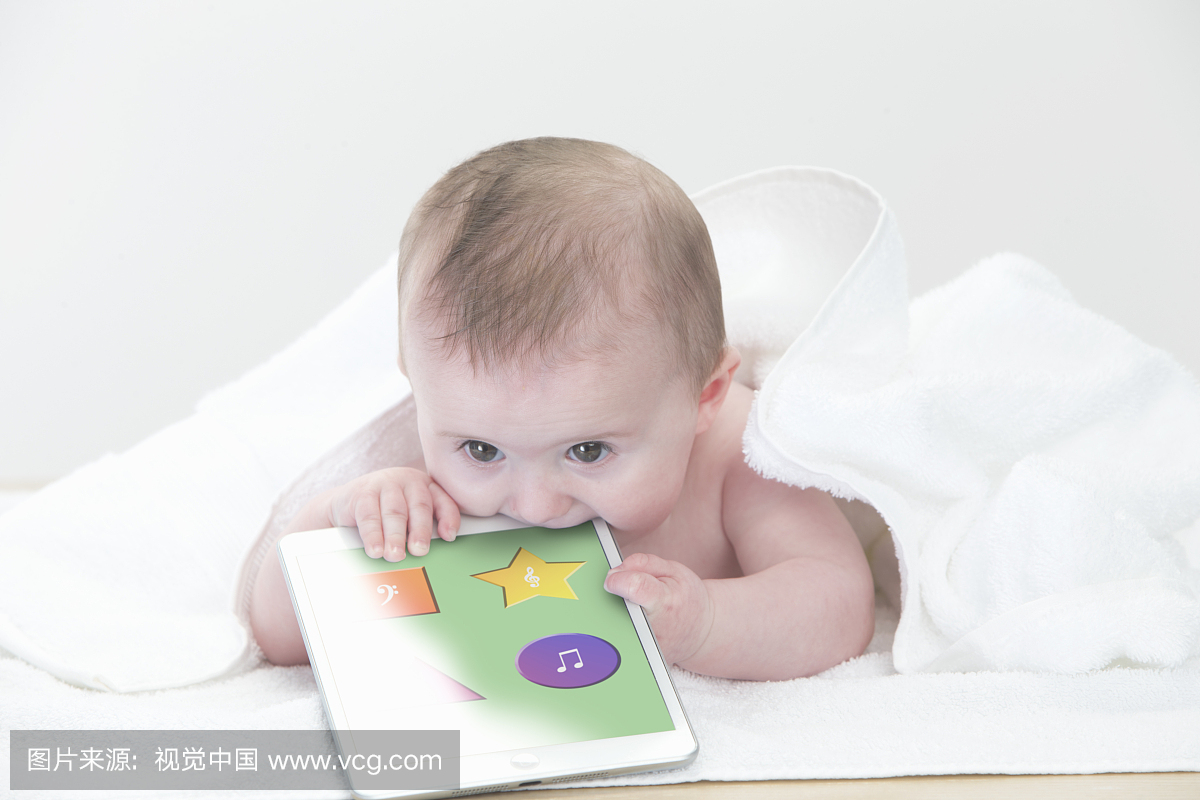 Baby laying on towel biting digital tablet