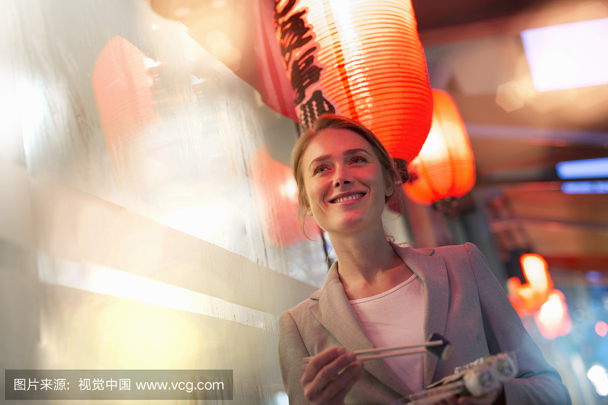 在晚上在城市街道上漫步的女人吃外卖寿司