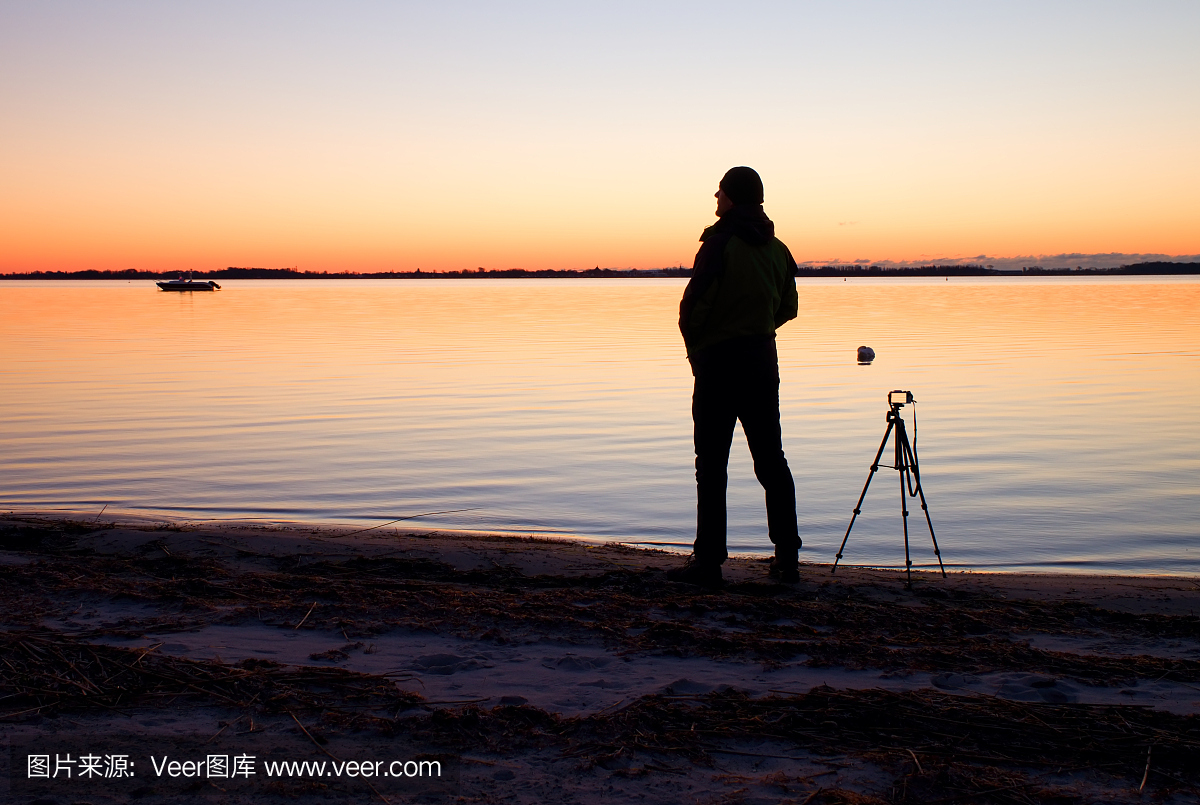 在三脚架高摄影师剪影拍摄在海滩上的照片